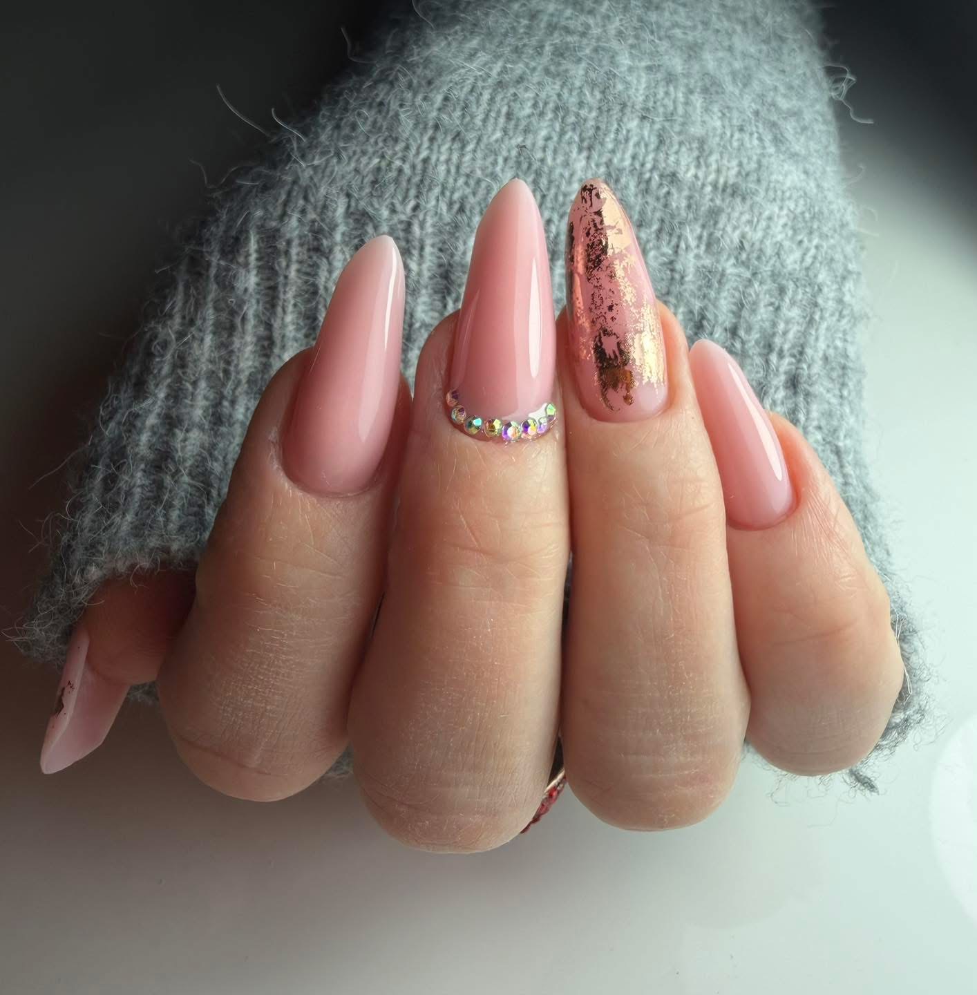 Lange nude amandelnagels met glitter en een folie-accent, hand in een grijze gebreide mouw