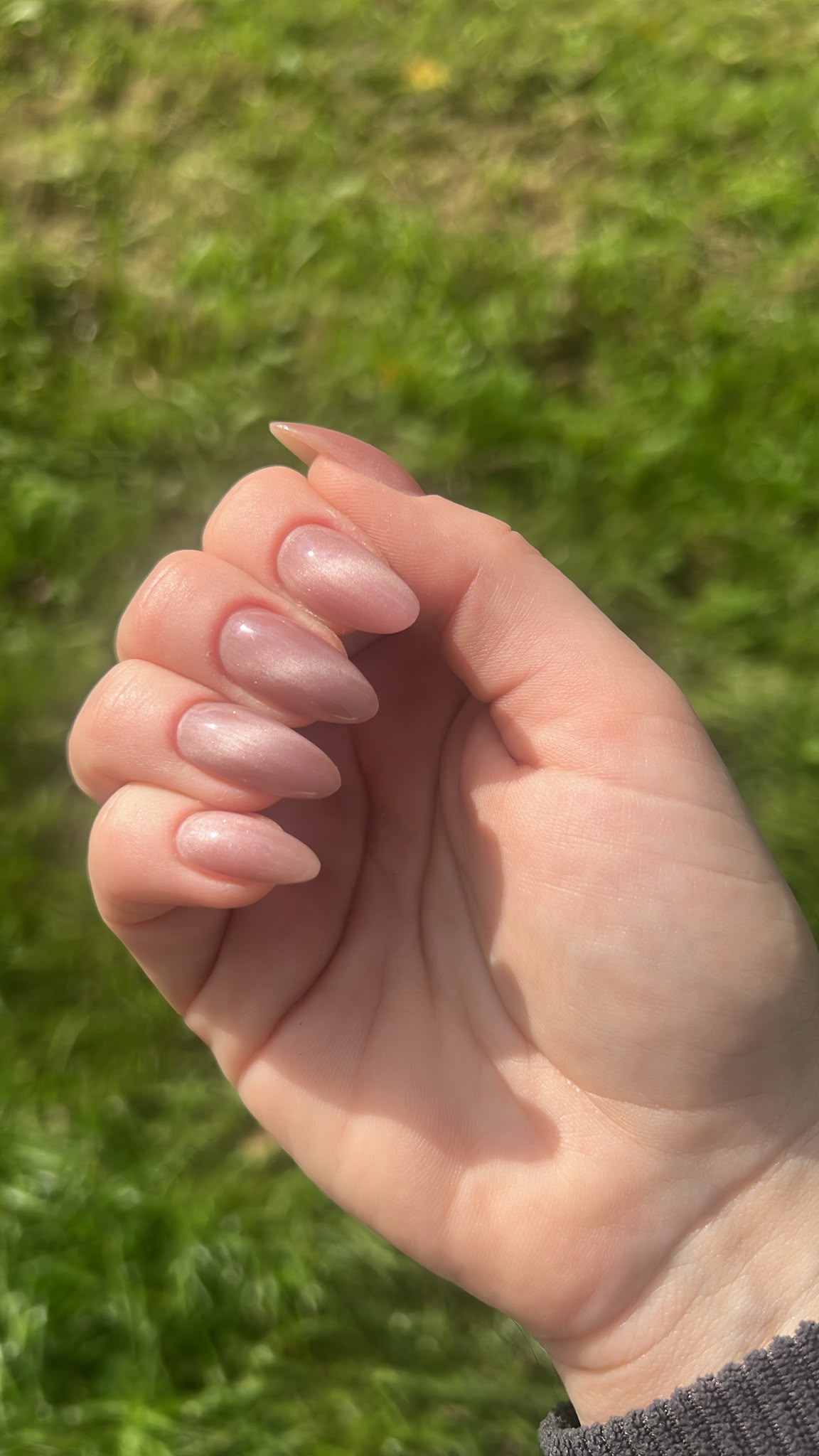 Nude amandelnagels, een hand voor een grasveld