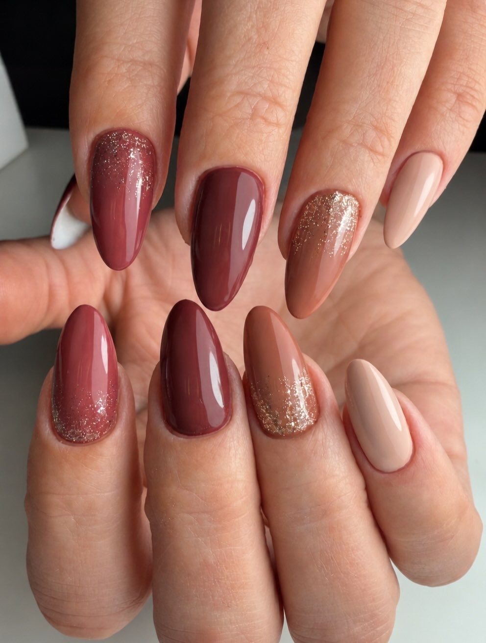 Amandelnagels in bordeaux, bruin en nude, met glitter op twee nagels