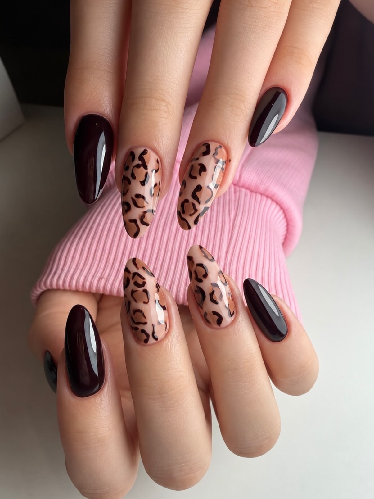 Amandelnagels met luipaardprint en donker bordeaux, handen op een roze mouw